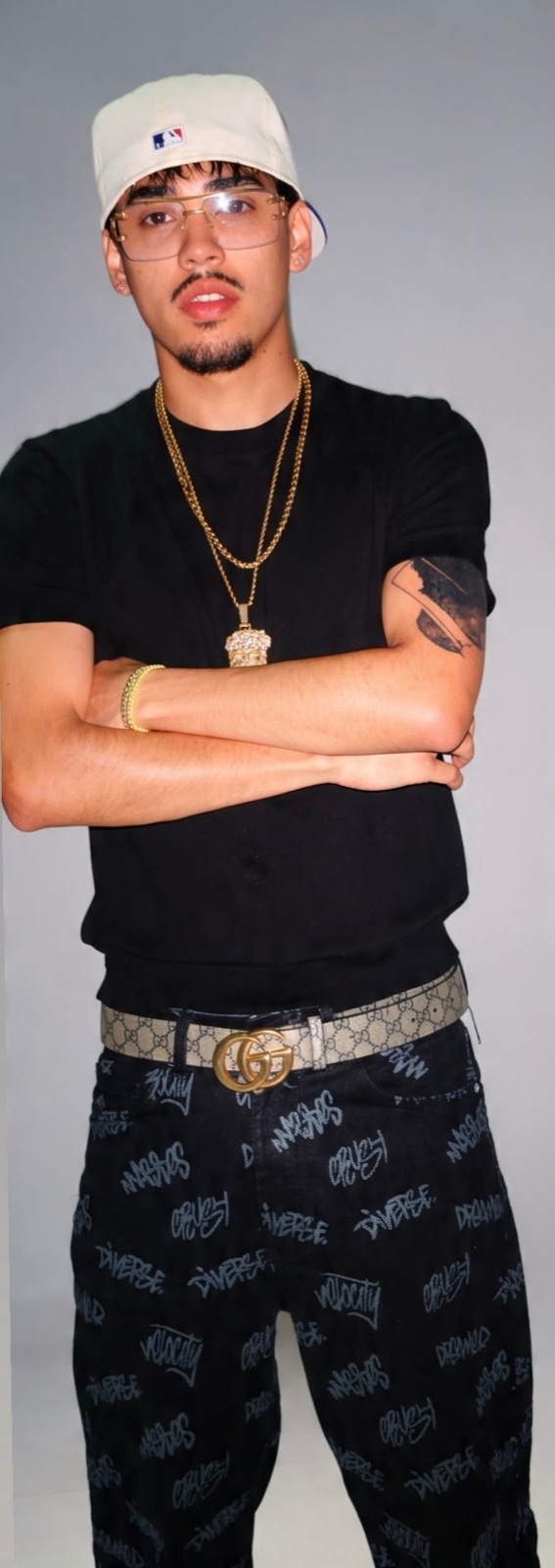 Retrato de estudio de Perseo con gorra, gafas y cadenas doradas, brazos cruzados